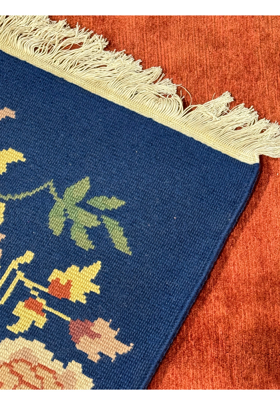 Close-up angled view of the corner of the modern Oriental Art Deco rug, highlighting the detailed floral design and the fringe on the navy border.