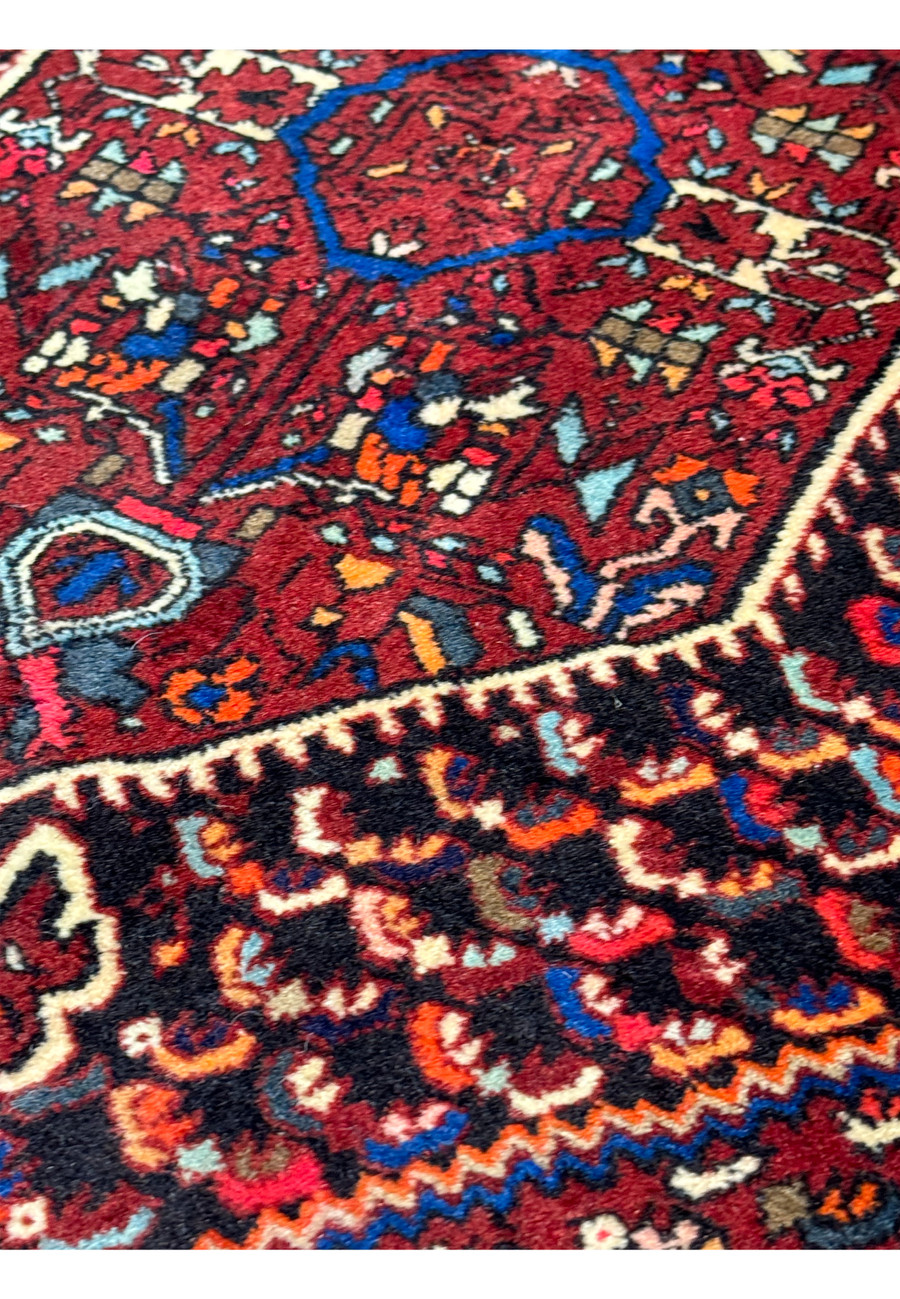Zoomed-in view of the dense, colorful floral and geometric designs on a 3 x 5 Persian Gholtogh rug, featuring shades of red, blue, and subtle touches of pink and green