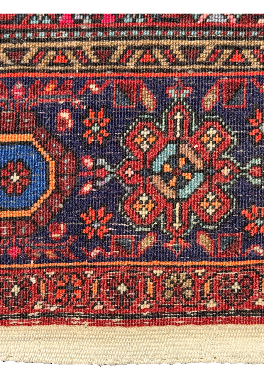 Close-up of the backside and fringe of a Persian Gholtogh rug, showing detailed patterns and color variations in red, blue, ivory, and hints of orange and green and weave density.