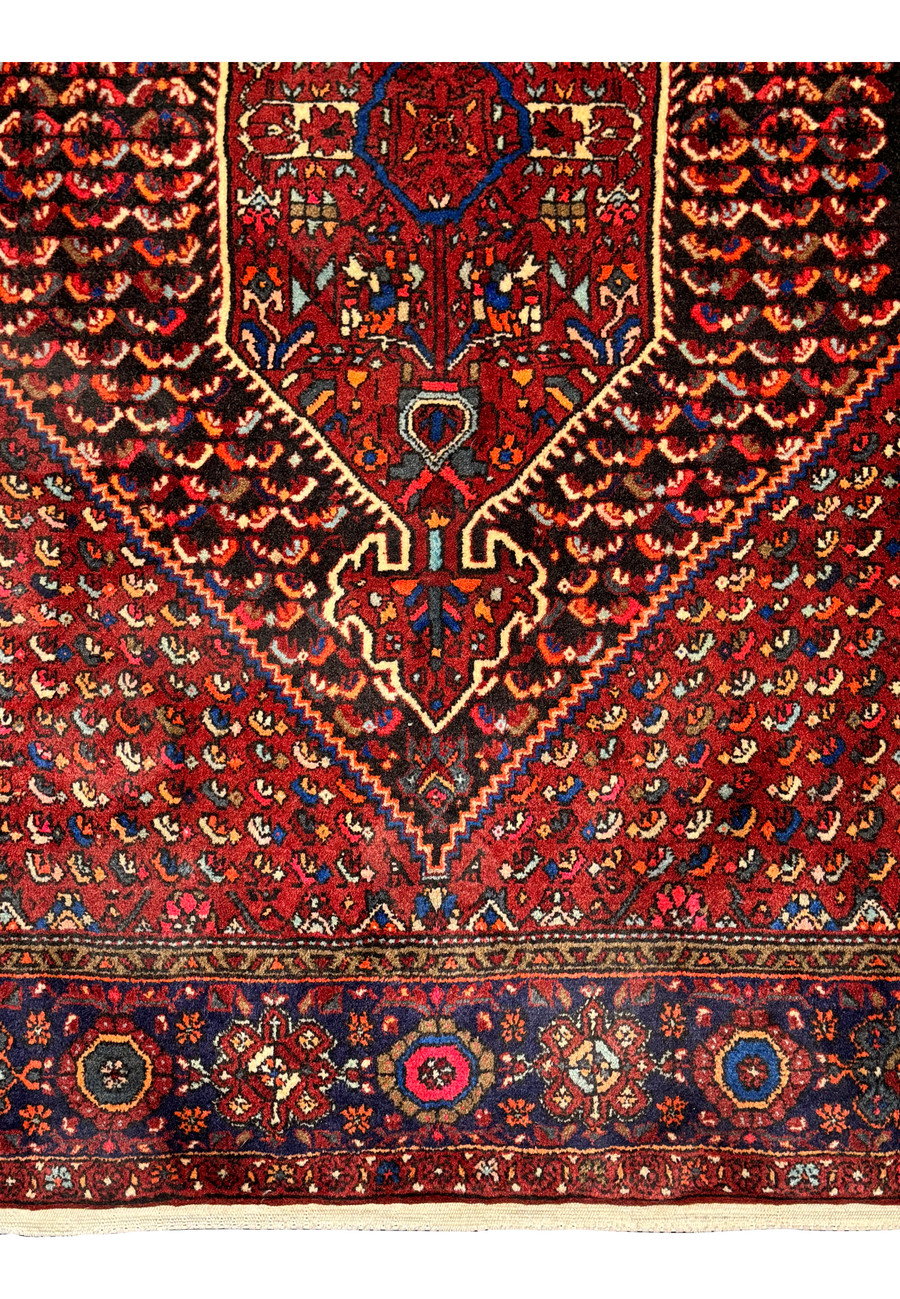 Macro shot focusing on the corner detailing of a Persian Gholtogh rug, showing the intricate craftsmanship of the floral and geometric patterns in a blend of red, navy, and ivory.