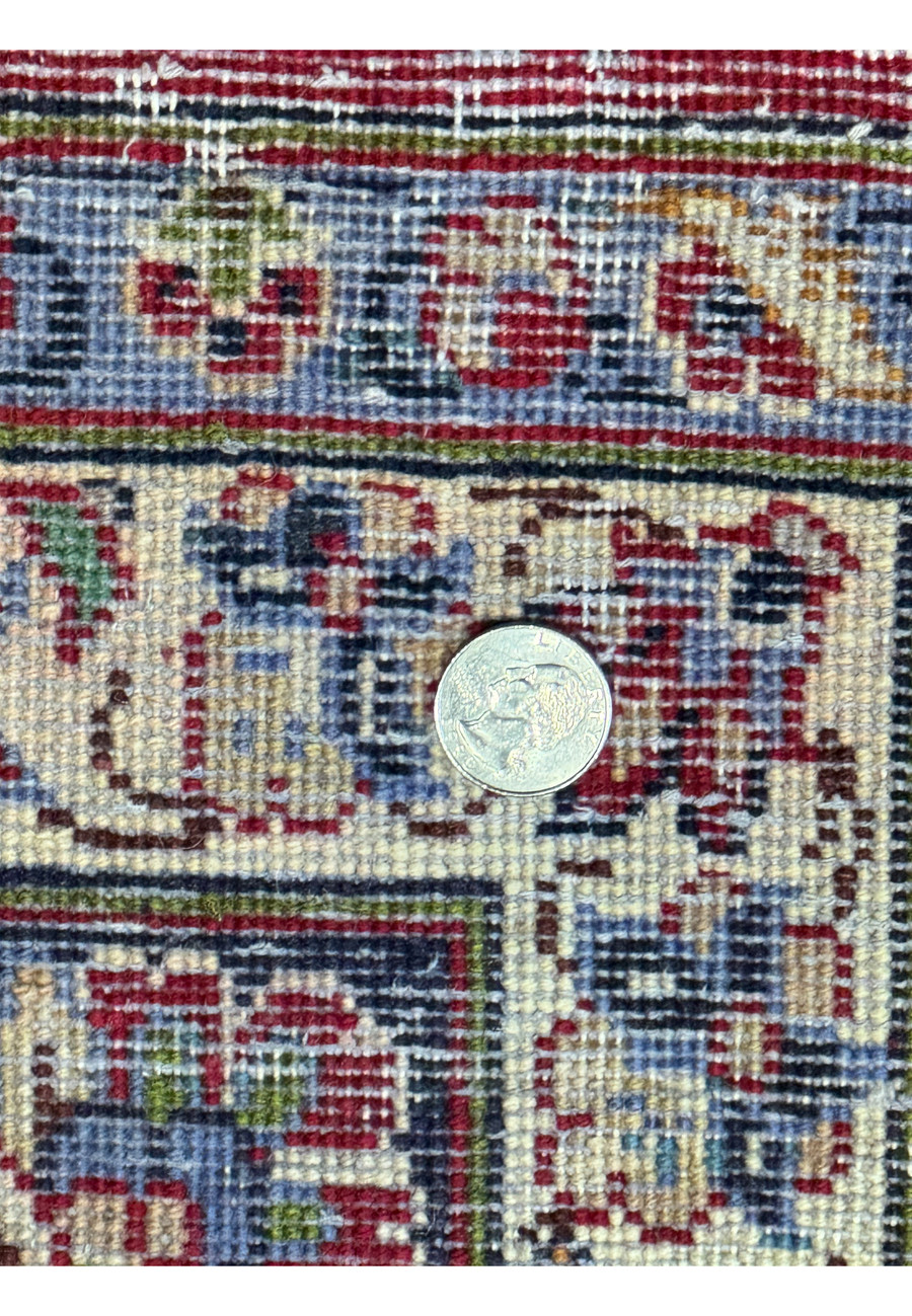 This image captures the reverse side of a finely woven Persian Isfahan rug. Quarter is placed on the rug to provide scale, emphasizing the high knot density and precision of the weave. The background shows a detailed texture comprising various colors, including deep blues, reds, and creams, indicative of the rug's complex design seen from the front.