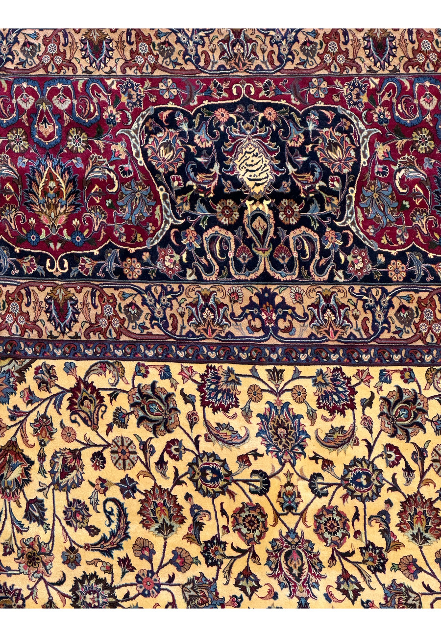 Close-up of the intricate patterns and vibrant colors in a Persian Mashad rug, featuring floral and vine motifs in red, blue, ivory, and gold, with detailed craftsmanship and traditional Persian design elements