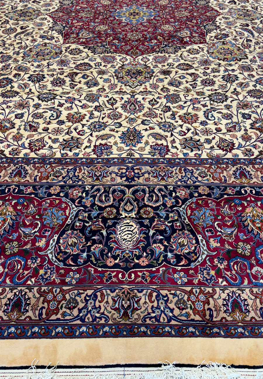 Focused view of the lower border of a Persian Mashad rug, showing intricate floral patterns and vine scrolls in deep red, blue, and ivory, with meticulous weaving and traditional Persian motifs