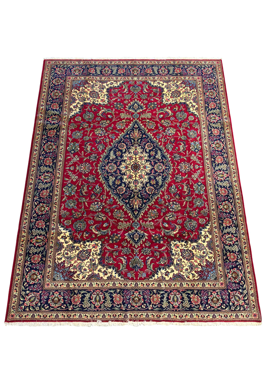 close-up view of the central medallion in a Persian Qum Kork Rug, showcasing intricate floral patterns in blue, cream, and gold on a rich red background.