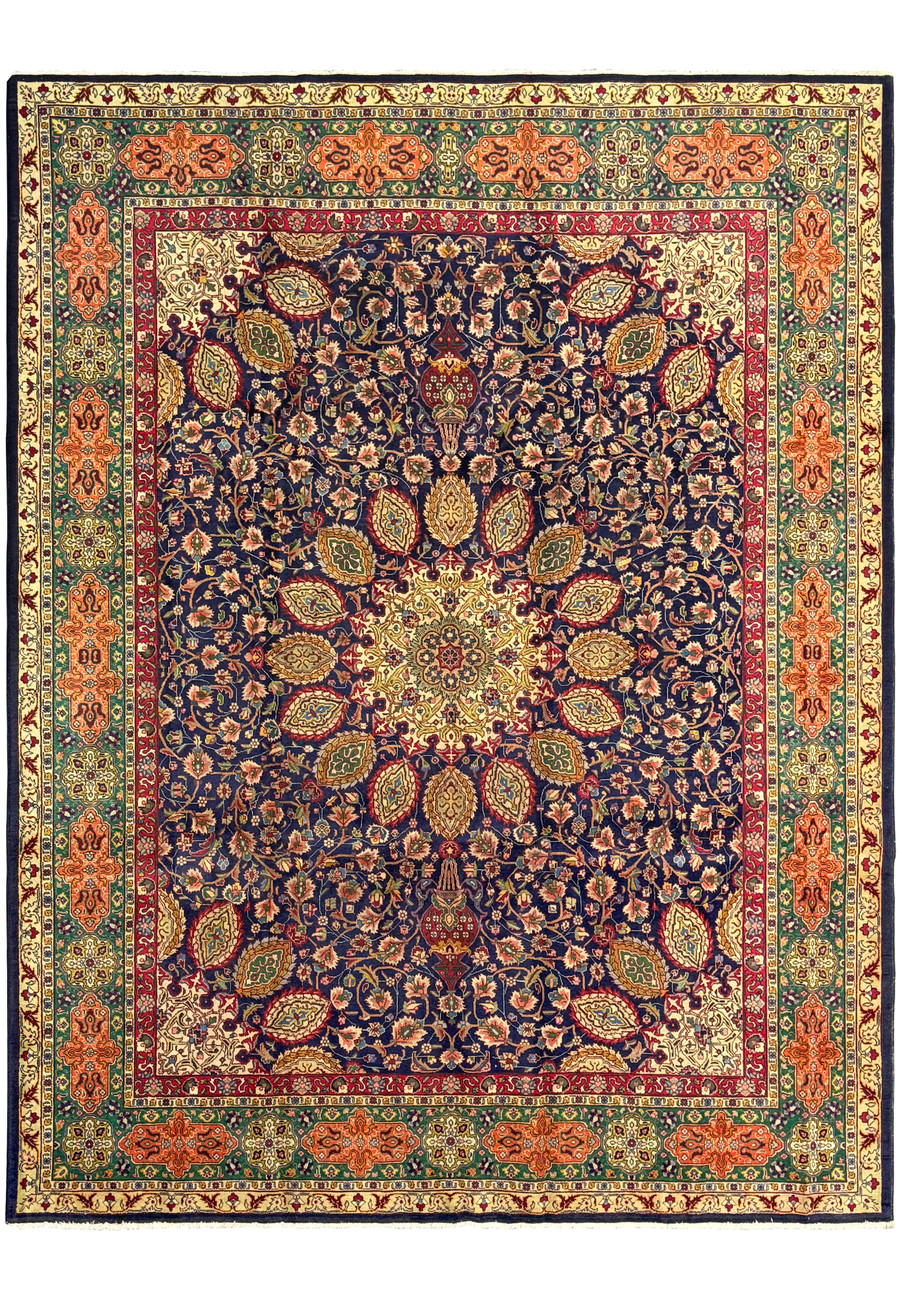 A close-up view of a Persian Tabriz Rug highlighting the intricate floral and medallion design. The rich navy blue background is adorned with vibrant red, green, and gold patterns, showcasing the meticulous craftsmanship and detailed knotting that are characteristic of Tabriz rugs. The central medallion is surrounded by an elaborate arrangement of flowers and leaves, adding to the rug's visual appeal and elegance.