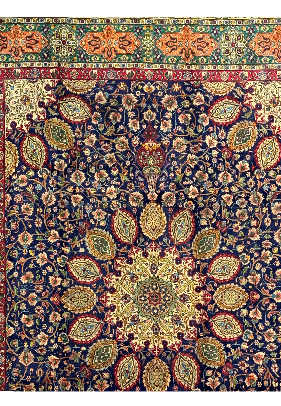 Close-up of the border of the Persian Tabriz Rug, displaying the geometric and floral patterns. The border features vibrant colors, including orange, green, and red, intricately woven to create a striking contrast against the navy blue field. The high-quality wool and dense knotting technique are visible, underscoring the rug's durability and artistic value.