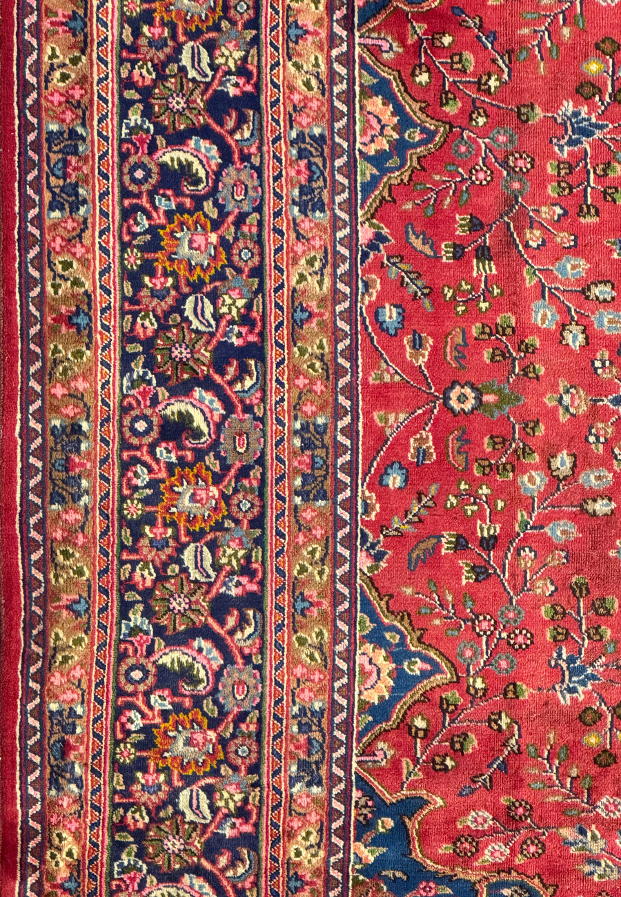 Perspective view of the Persian Mashad rug showing its overall design and detailed border.