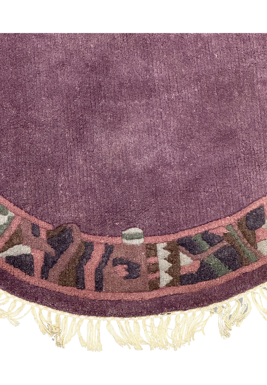 Detailed view of the geometric motifs in muted rose and olive green on the border of the round Nepalese rug.