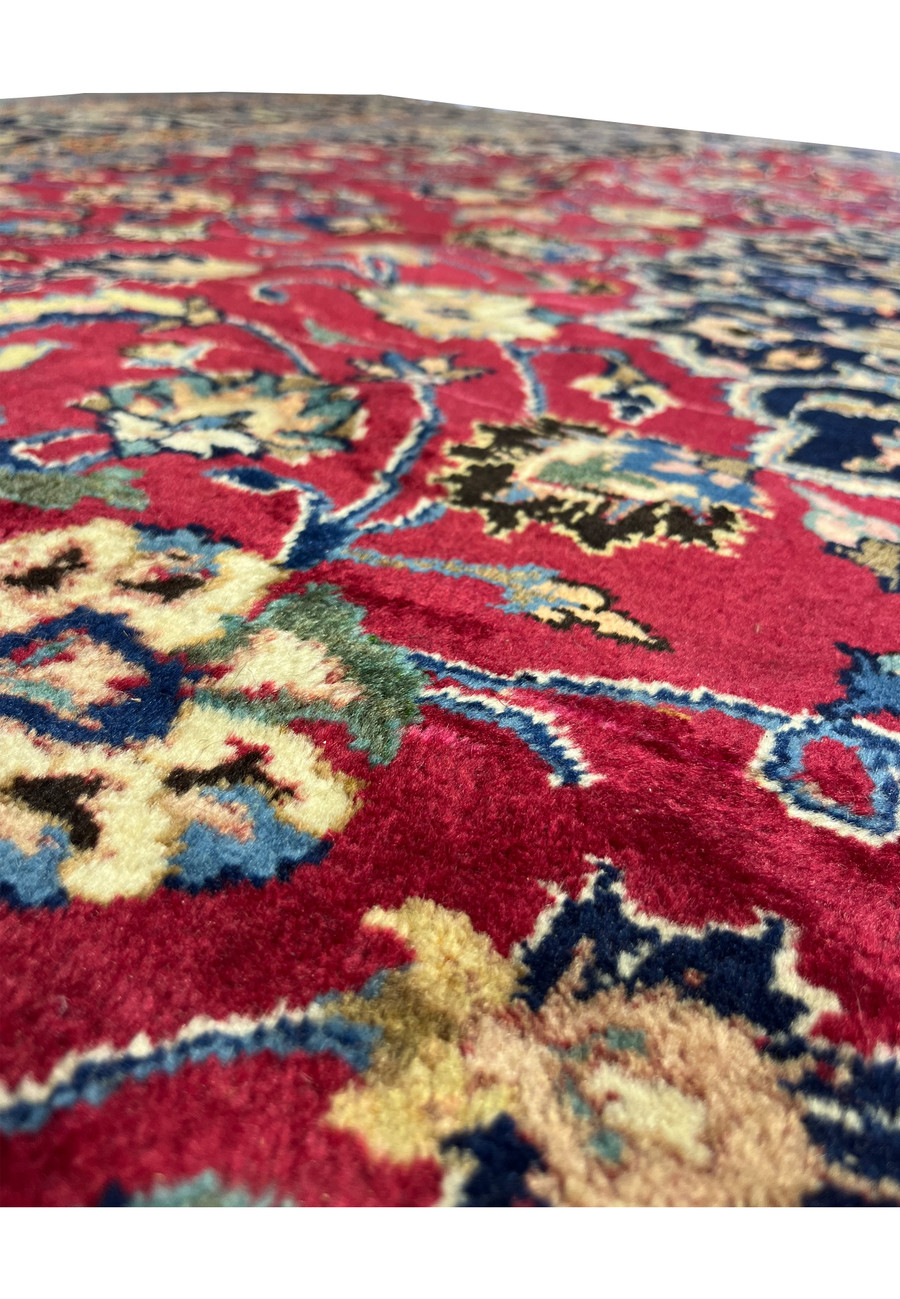 Close-up of vibrant red field and floral motifs on Persian Mashad Rug highlighting wool texture
