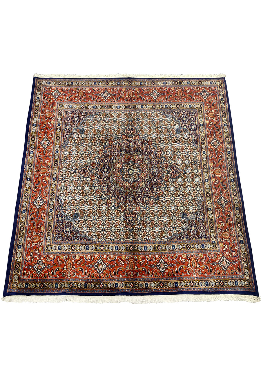 Laid-down view of the Persian Moud rug displaying its precise geometric symmetry, navy medallion center, and fine handknotted motifs across an ivory and rust-red color palette.