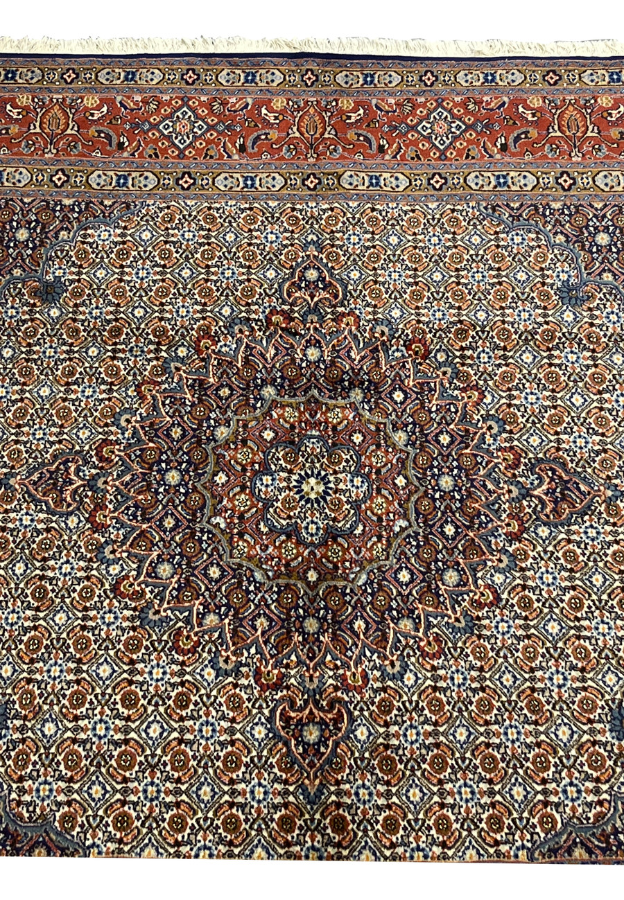 Detailed shot of the medallion with deep navy and rust tones framed by ivory petals, showing the classic Moud composition blending symmetry and fine color gradation.