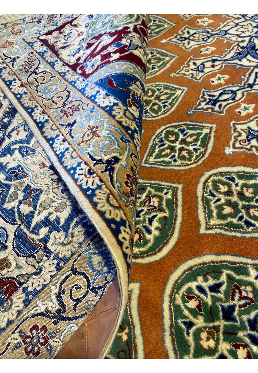Rolled presentation of the 9x9 Persian Nain 6La rug showing its flexibility, sheen, and rich rust-and-blue tones, demonstrating the luxurious silk highlights and tight hand-knotted quality.