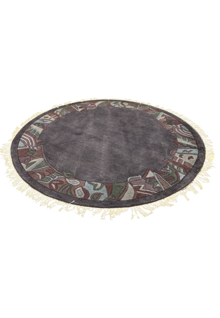 Side view of the round 5'3 x 5'3 Nepal rug highlighting its dense hand-knotted wool pile, raised border pattern, and soft beige fringe on a smooth gray field.