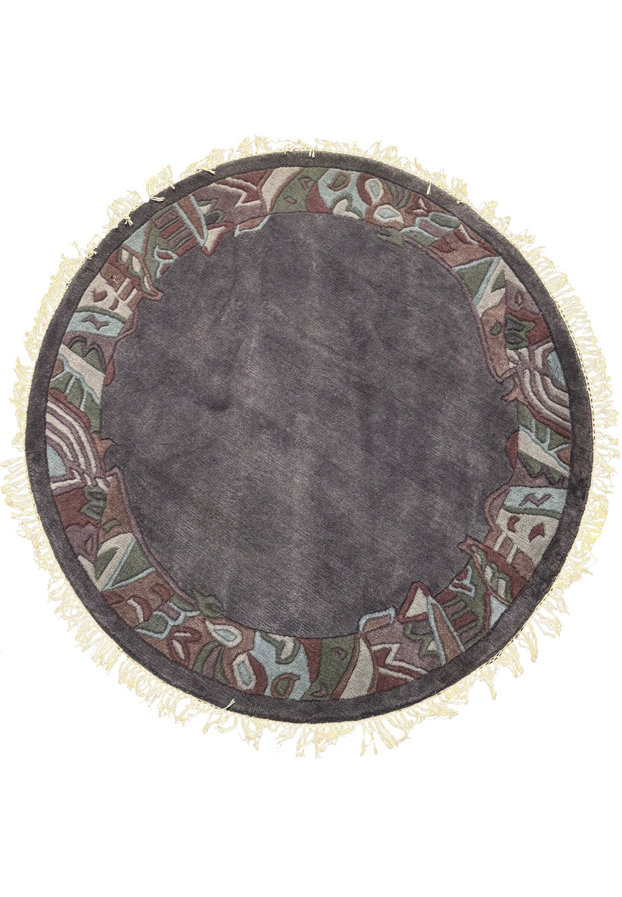 Full top-down view of the 5'3 x 5'3 Round Modern Nepal Rug showcasing its charcoal-gray wool field and hand-carved abstract border in olive, burgundy, and blue tones with light fringes.