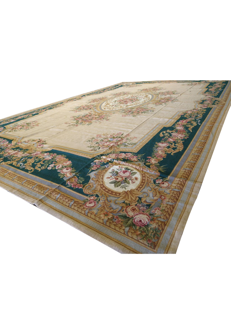 Angled perspective of a large French Aubusson rug showing emerald green border, floral garlands, beige field, and refined European symmetry