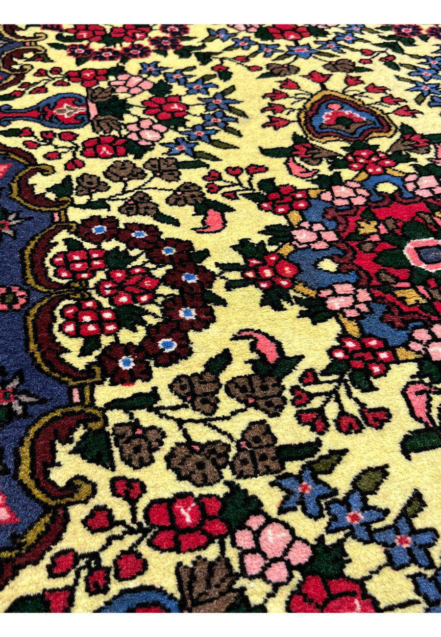Detailed close up of Persian Bijar rug field showing golden yellow wool, floral patterns, vine scrolls, and precise hand knotted craftsmanship