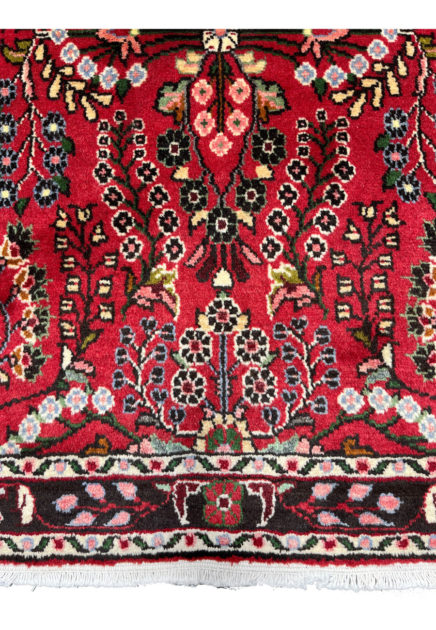 Lower border detail of a Persian Darjazin rug highlighting floral guard borders, rhythmic vine motifs, ivory highlights, and strong color contrast against the red field