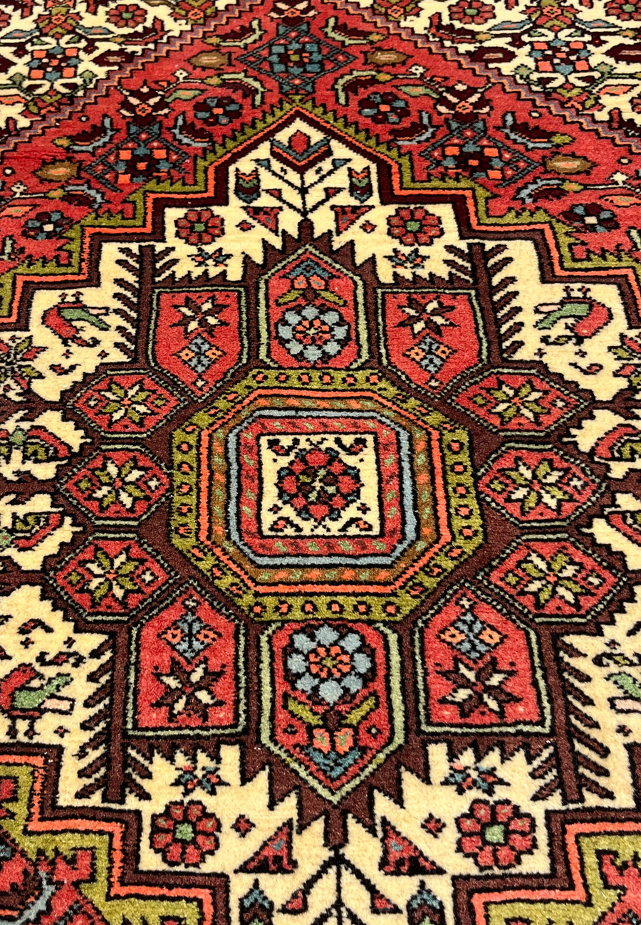Midfield detail of Persian Gholtogh rug showing angular floral motifs on brick red background.