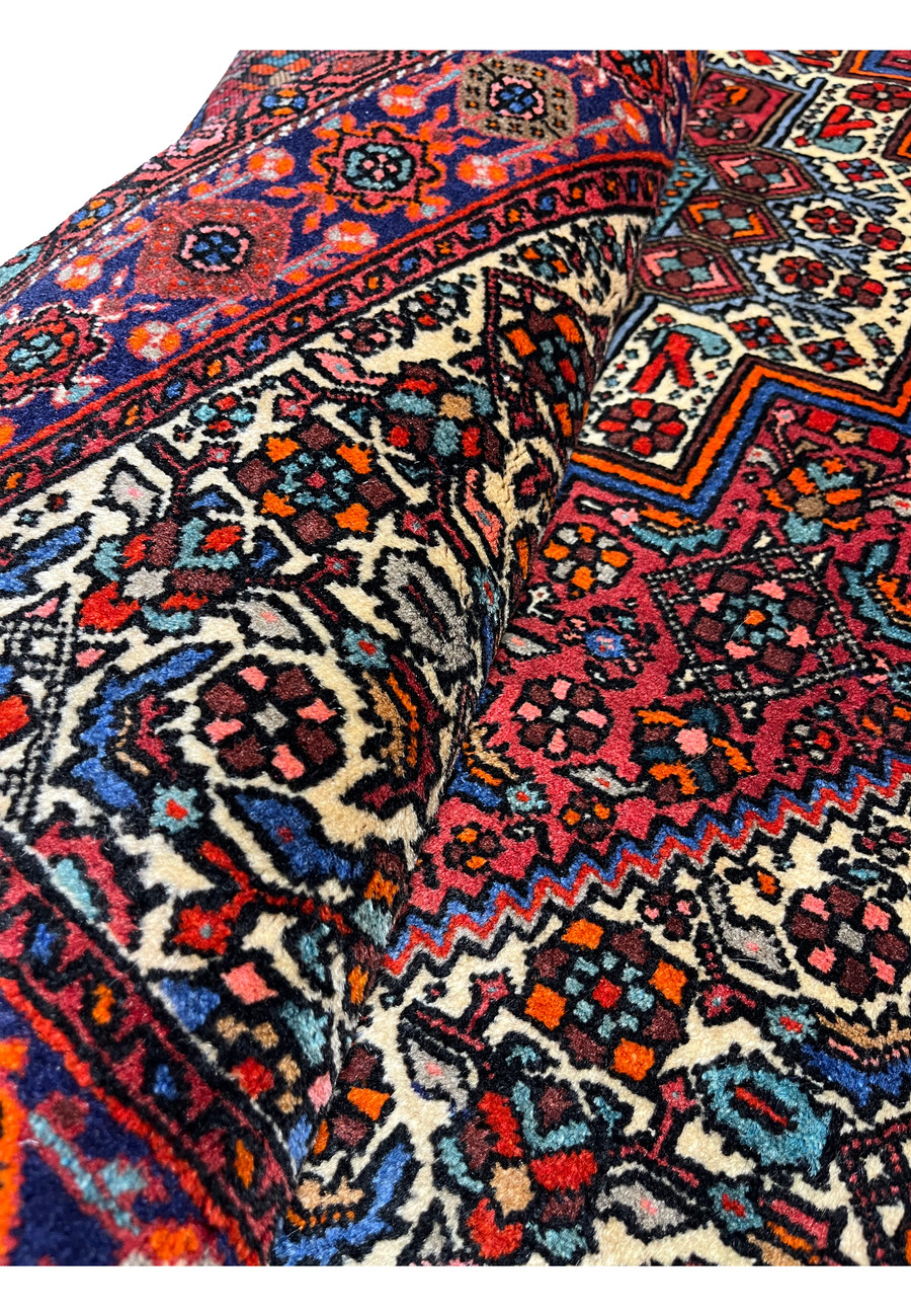 Rolled Persian Gholtogh rug showing wool thickness, flexibility, edge finish, and vibrant color saturation across geometric patterns