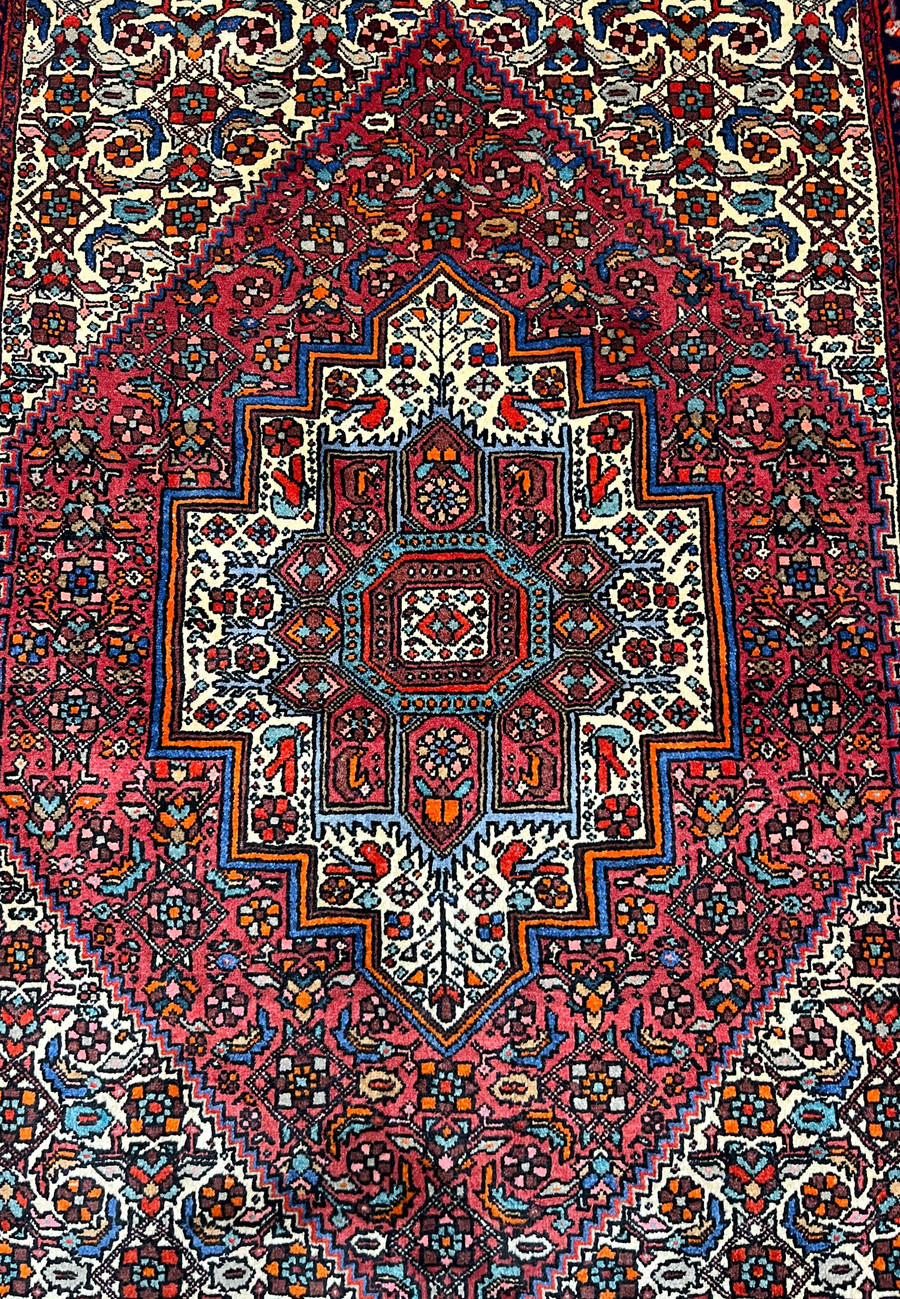 Close-up of the central geometric medallion in a Persian Gholtogh rug, highlighting precise knotting, stepped outlines, rich red tones, and ivory contrast