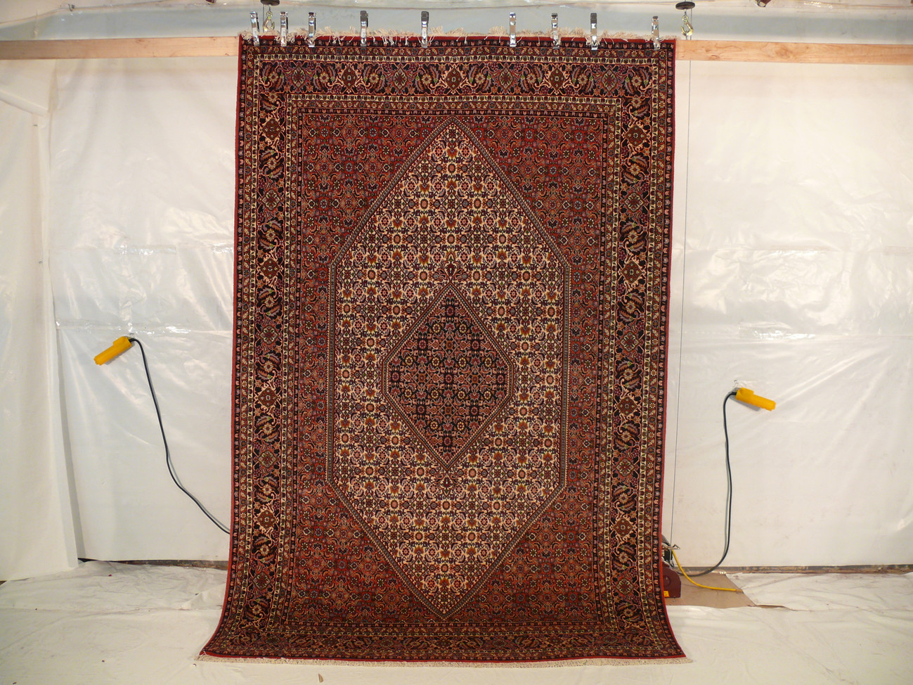 Hanging view of a 6'5 x 10 authentic Persian Bijar rug showing its firm iron rug structure, dense wool pile, crisp medallion design, and rich red color tones