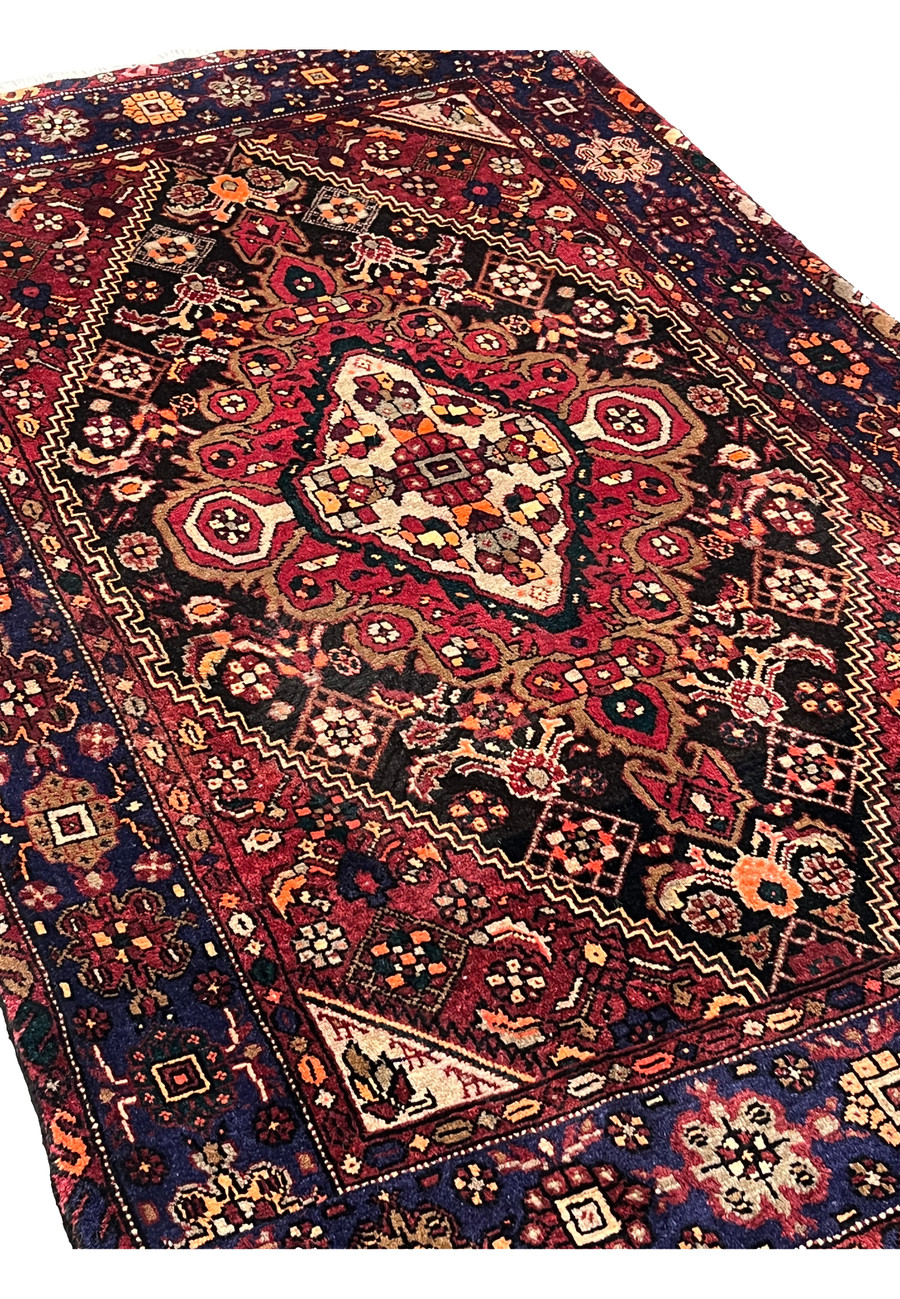 Angled view of a Persian Gholtogh rug showing pile height, saturated colors, bold medallion layout, and sturdy village weaving