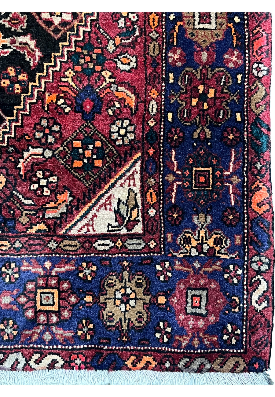 Border close-up of a Persian Gholtogh rug highlighting dense wool weave, bold tribal symbols, navy background, and warm accent colors