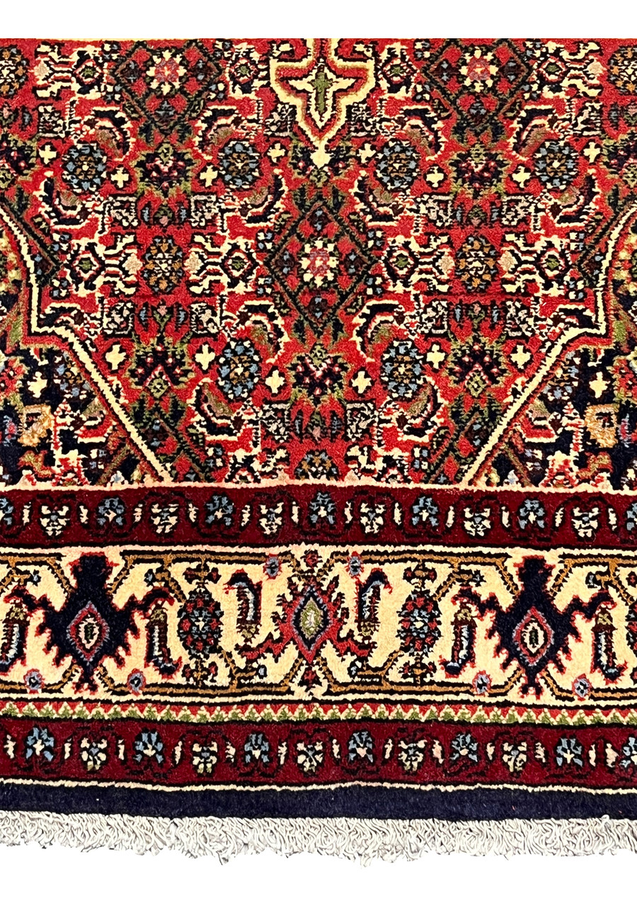 Lower border view of a Persian Bijar rug featuring layered framing, deep red tones, floral rosettes, and strong visual definition