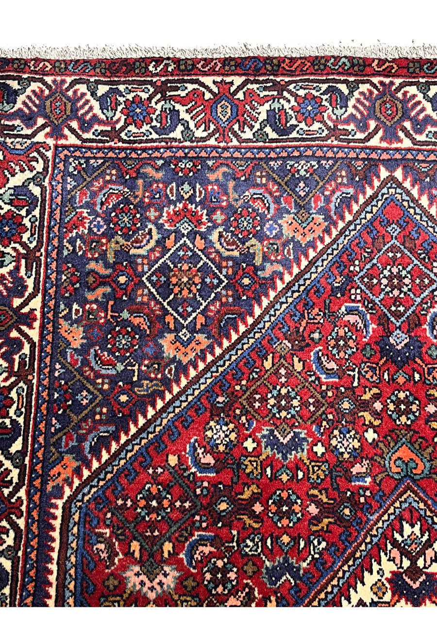 Inner border detail of a Persian Gholtogh rug showing precise geometric framing, ivory highlights, and deep red to navy color transitions.