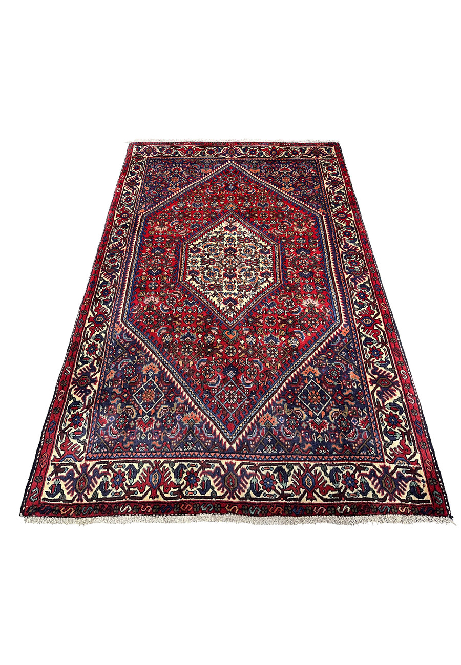 Hand-knotted Persian Gholtogh rug laid flat showing strong tribal symmetry, deep red background, ivory medallion, and dense village weaving.