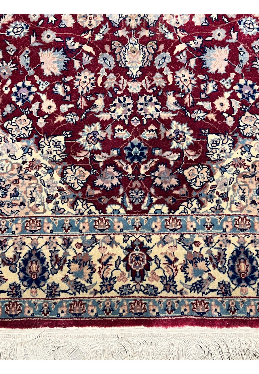 Lower section of Persian Tabriz rug with burgundy field, balanced floral composition, and traditional border elements near the fringe