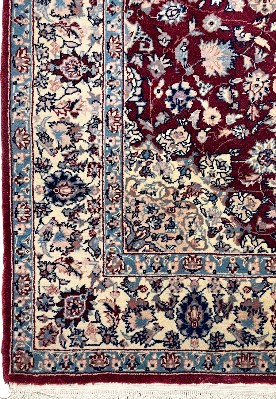 Border close up of Persian Tabriz rug displaying floral rosettes, light blue framing, ivory background, and crisp hand knotted detail