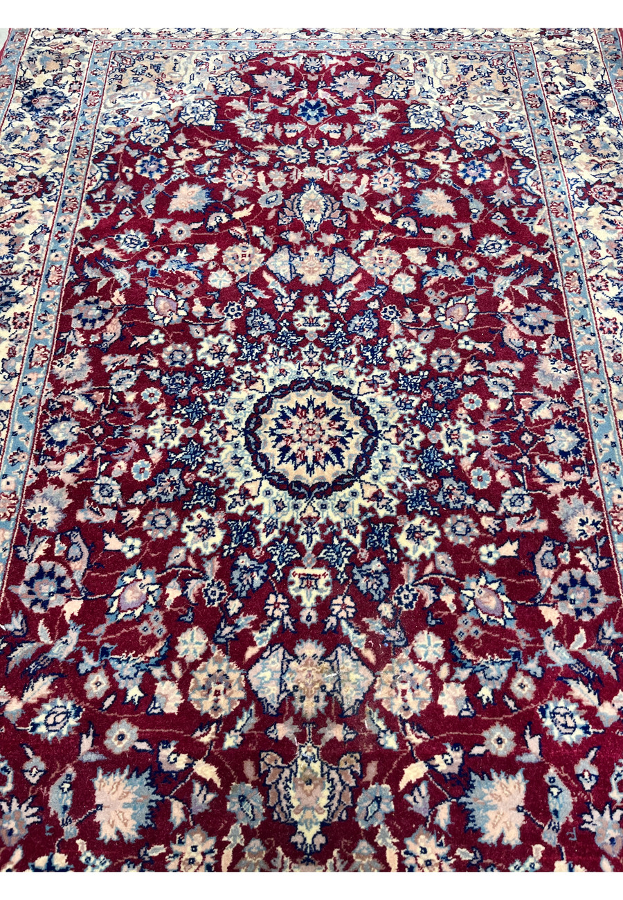 Midfield detail of Persian Tabriz rug highlighting burgundy background, symmetrical floral motifs, and precise hand knotted craftsmanship