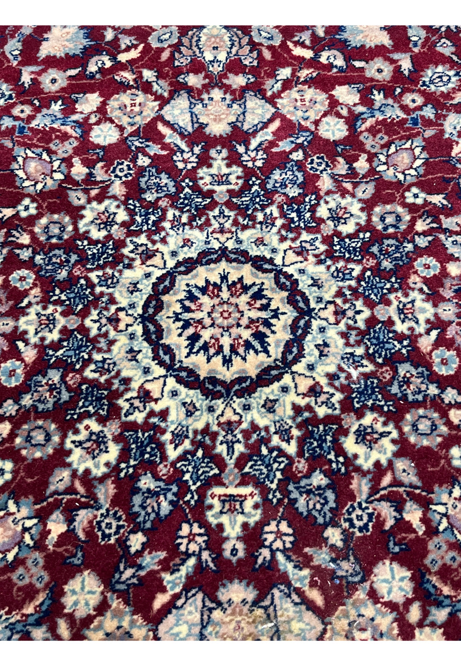 Central medallion close up of Persian Tabriz rug with burgundy field, ivory starburst design, navy blue outlines, and fine wool texture