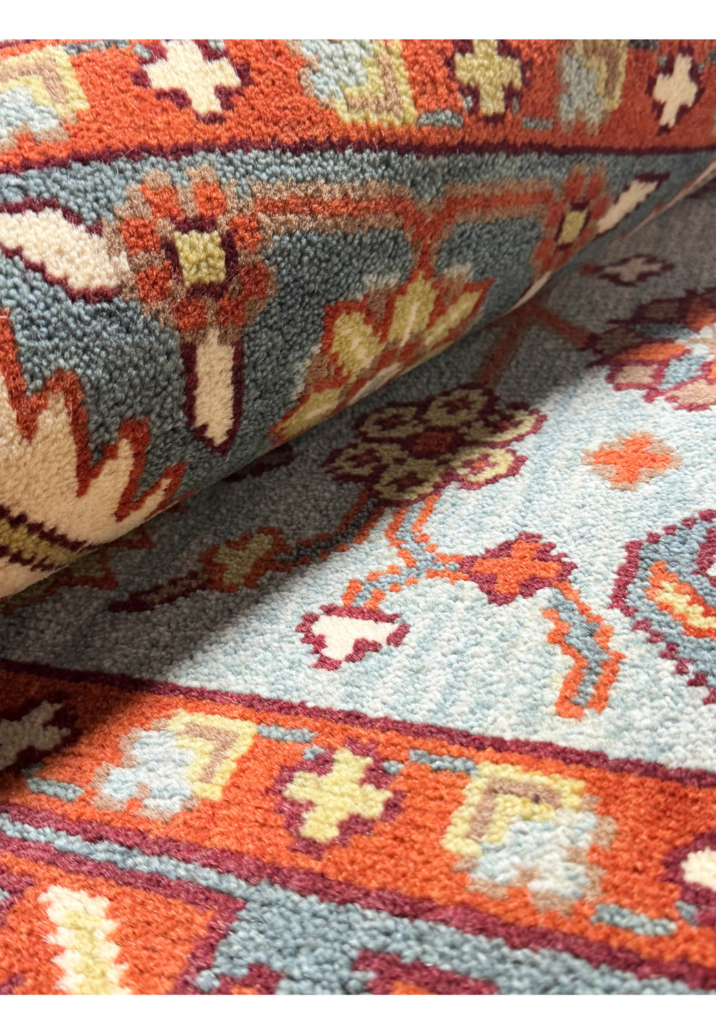 A side angle view of a folded 8x8 Oushak rug, showcasing the thickness and soft texture of the weave, with a glimpse of the intricate patterns and color combination