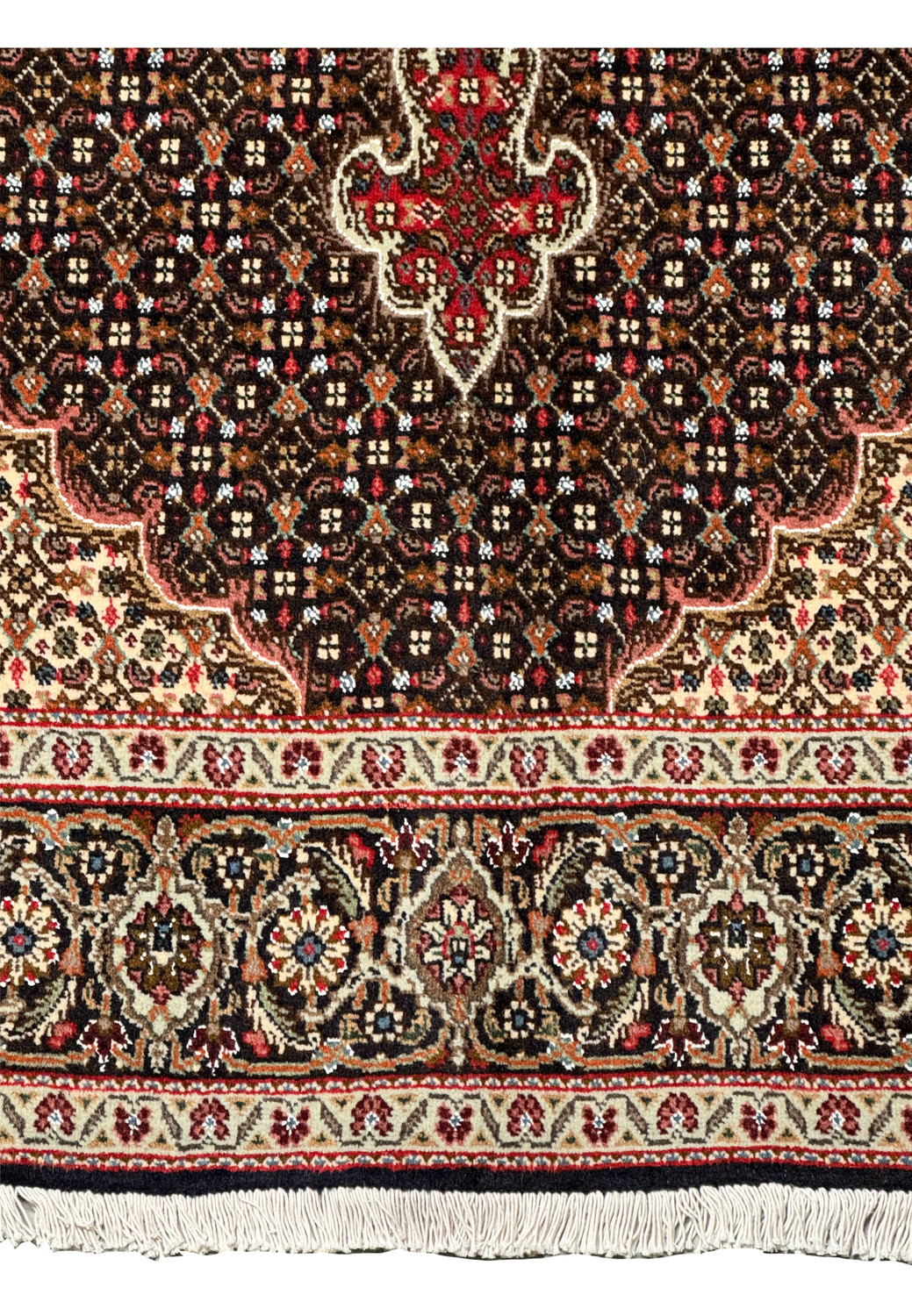 Close-up of the corner of a Persian Tabriz Mahi rug, highlighting the fine craftsmanship of the cream and beige floral motifs on a dark brown background