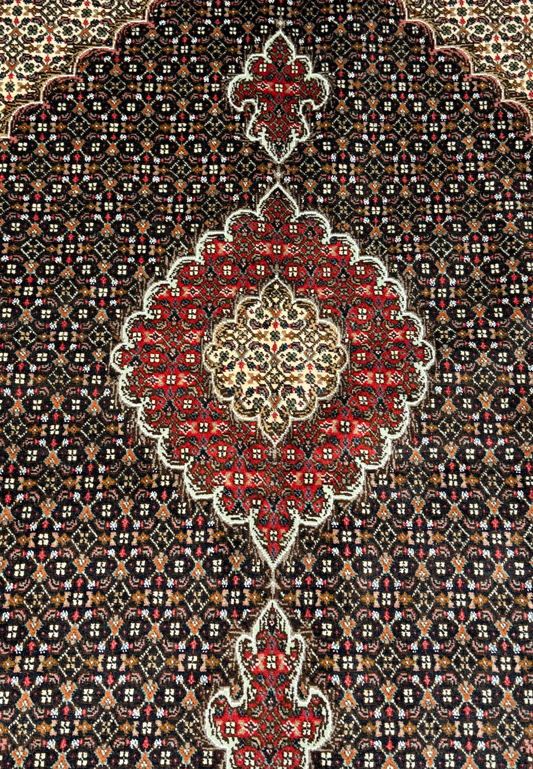 Close angled view of a Persian Tabriz Mahi rug, emphasizing the dense weave and rich color palette with a dominant dark brown field.