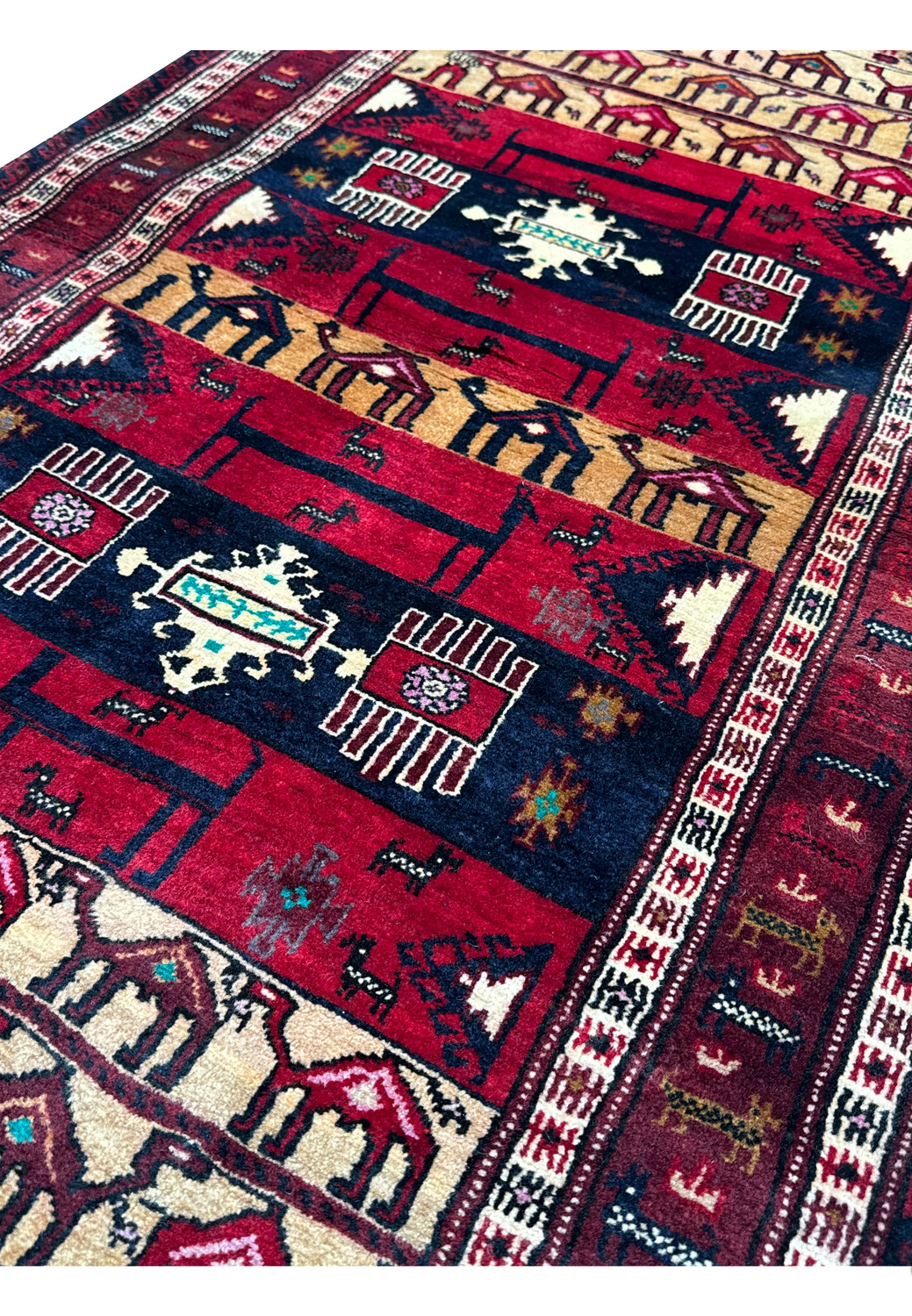 Angled close-up showcasing the texture and weave of a Persian Baluch Tribal rug with deep red and dark blue patterns