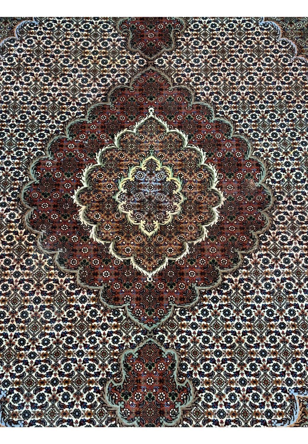 Detailed view of the central medallion of a Persian Tabriz Mahi rug, emphasizing the dense floral pattern and rich color palette on a dark field, with highlights of silk giving a subtle sheen.