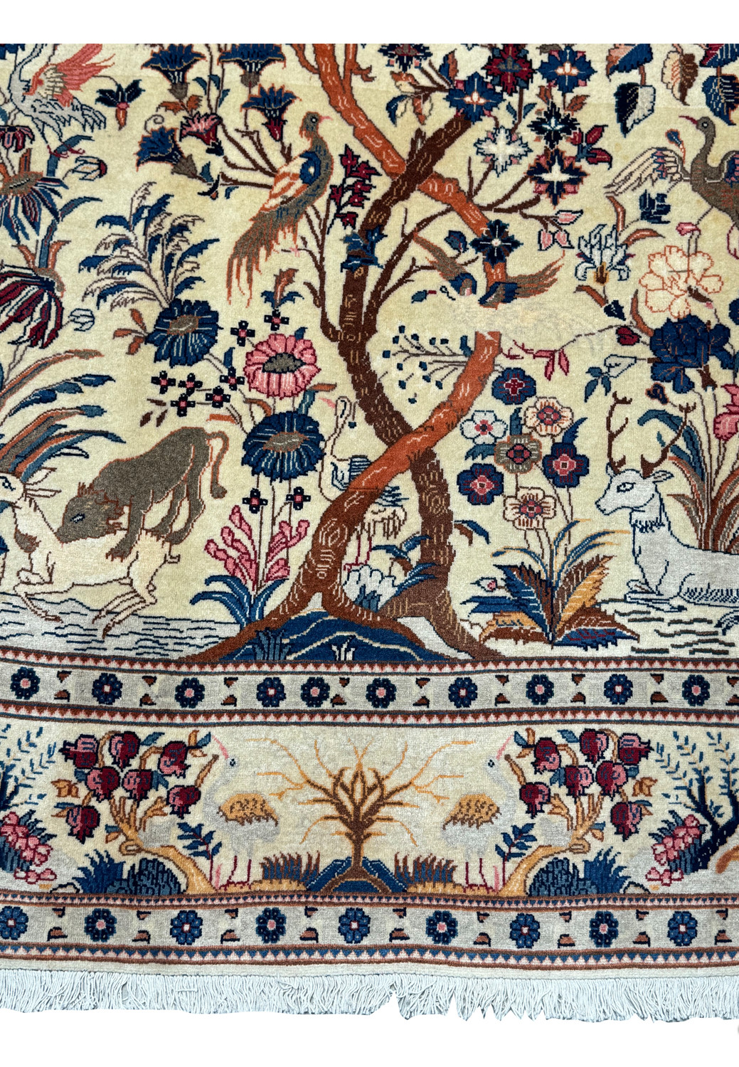 Detailed view of the lower section of a century-old Persian Kashan rug, focusing on the Tree of Life's base with animal interactions and intricate floral patterns