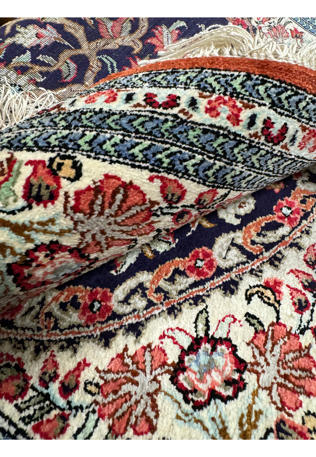 Folded corner of the Persian Qum silk rug revealing the rug's thickness and the intricate design continuity