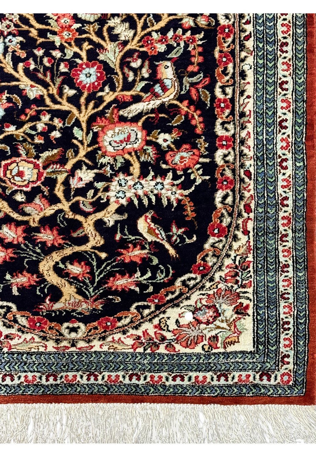 Edge of the Persian Qum silk rug, highlighting the tight weave, fringe details, and contrasting border colors