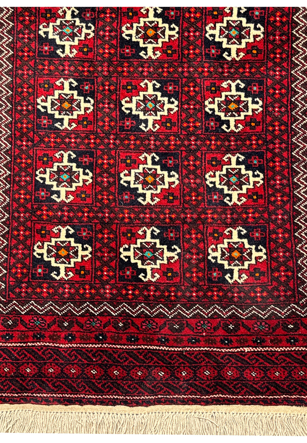 Full view of a Persian Baluch area rug, emphasizing the rich red field, traditional motifs, and natural wool fringes.