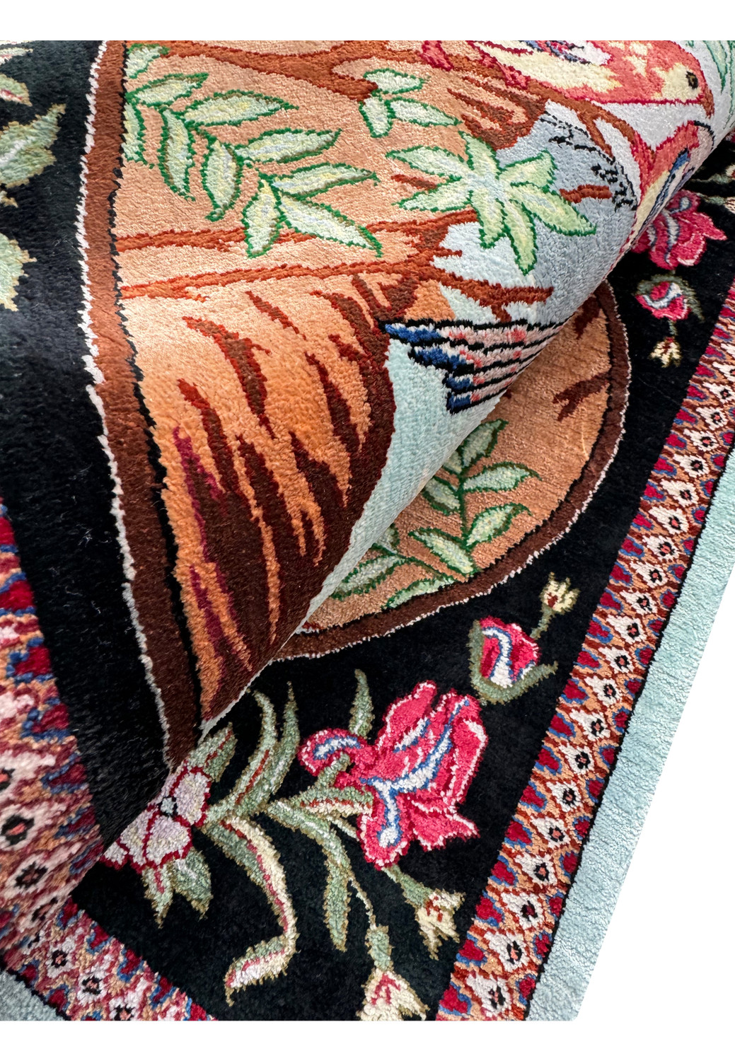 A corner detail of a Persian Qum silk rug, showcasing the fine weave and vibrant colors of the floral border