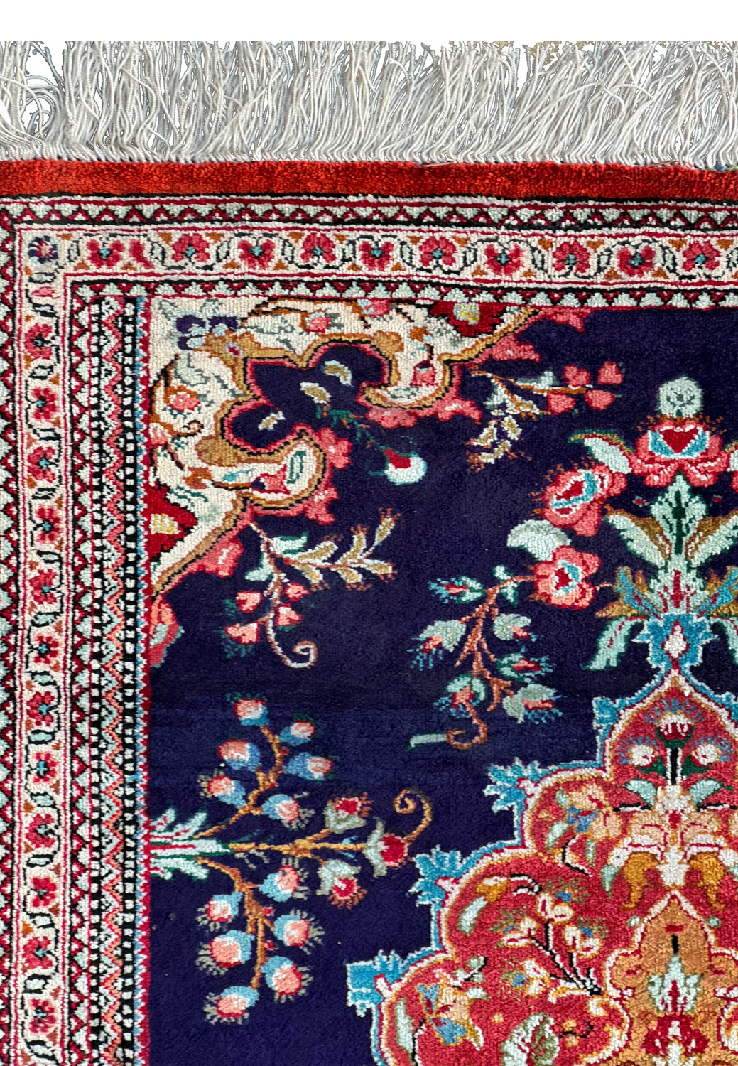 Edge of a Persian Qum silk rug with a close-up on the fine fringe and the ornamental border