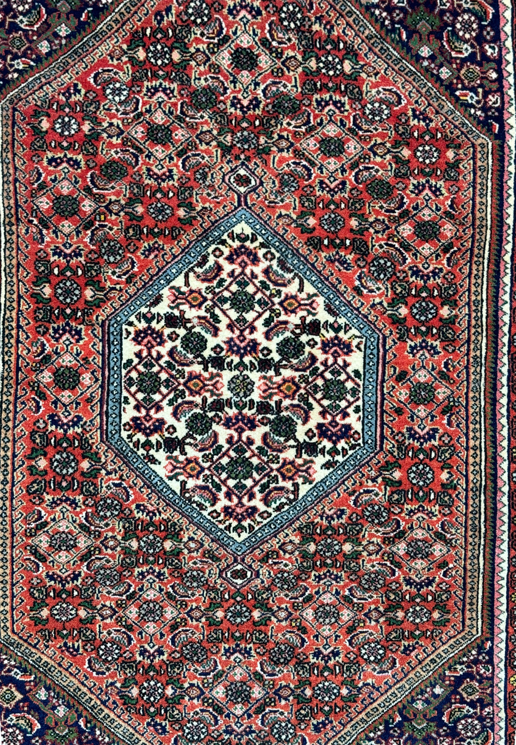 Close-up of the central medallion on a Persian Bijar Rug with detailed floral motifs in crimson red and cream on a navy blue background