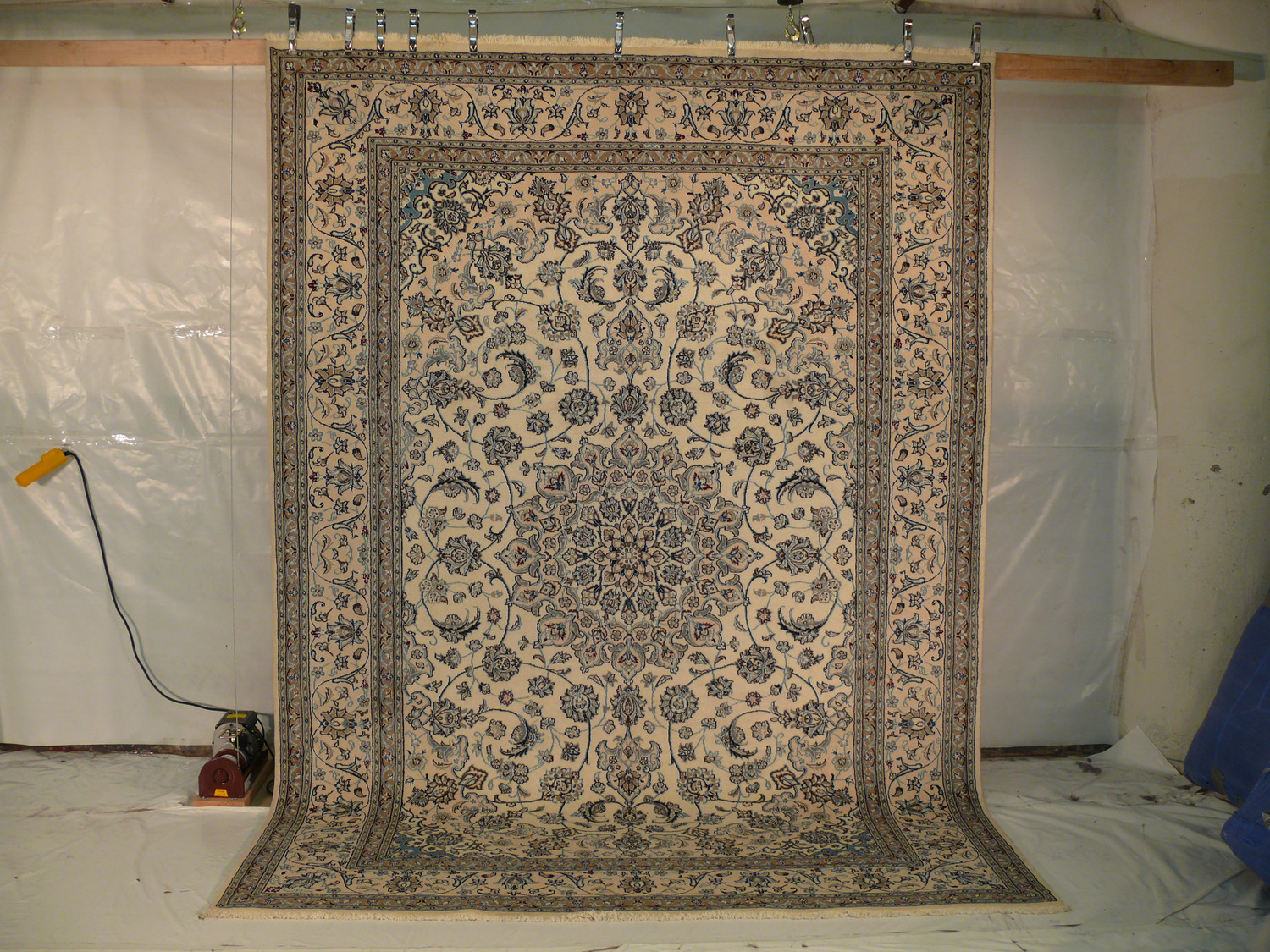 Handmade Persian Nain rug laid flat with beige field, navy medallion, and floral borders Handmade Persian Nain rug laid flat with beige field, navy medallion, and floral borders