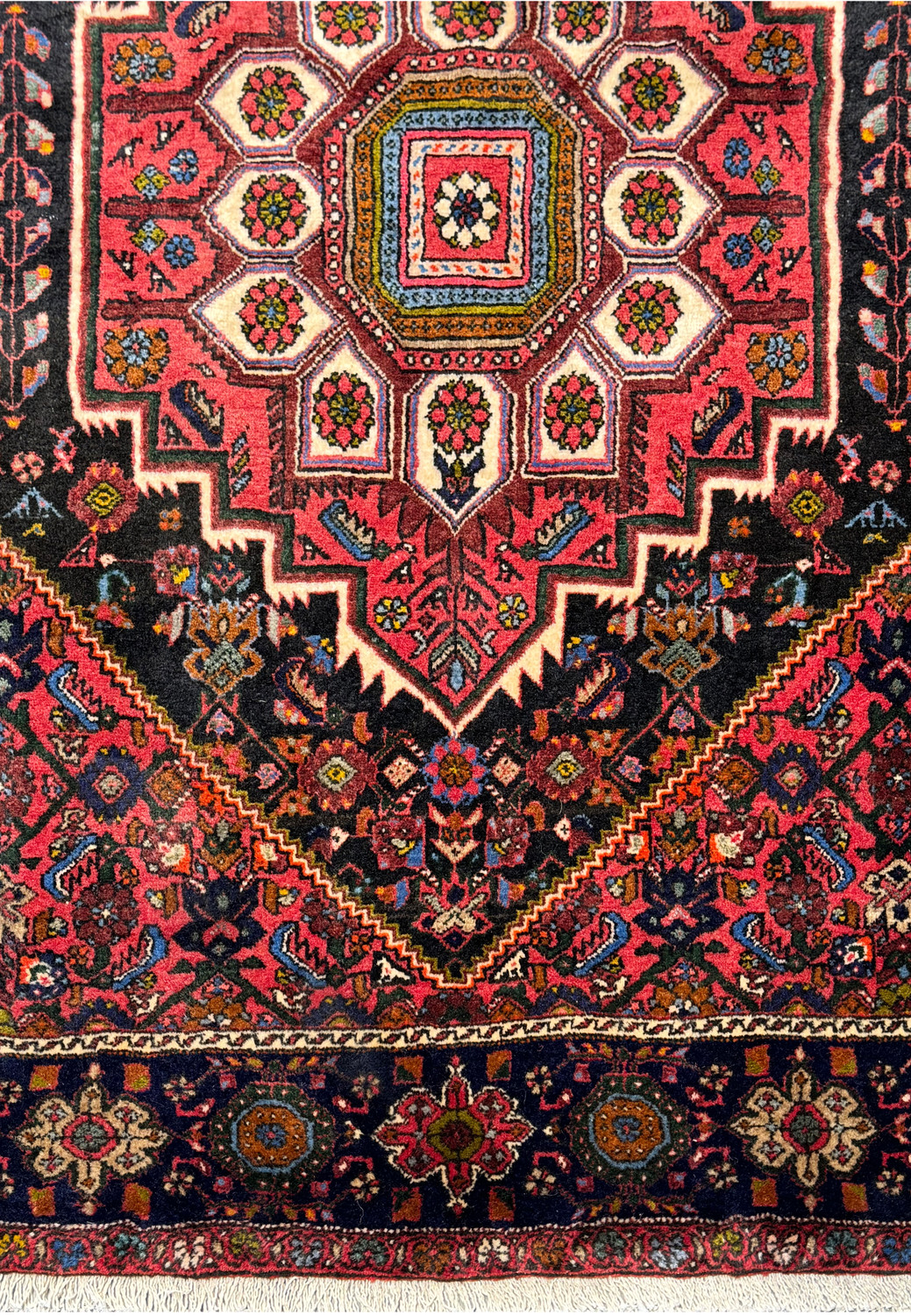 Angle view of the Persian Gholtogh rug showing the depth of the pile and the vibrant contrast between the red field and blue border.