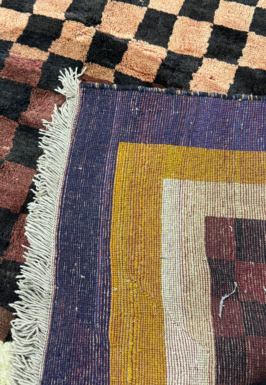 Detailed image of the corner of a modern Nepal rug, showing the fringe and the transition between the checkerboard center and the bold border colors.