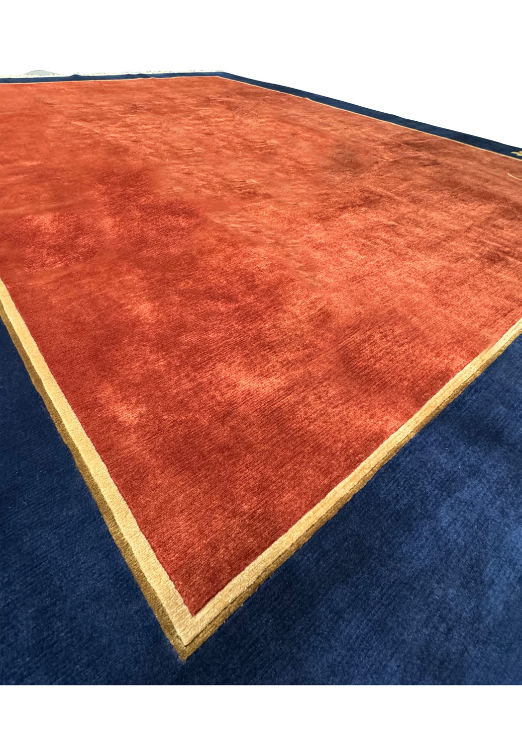 Close-up angled view of the modern Oriental Art Deco rug highlighting the contrast between the burnt orange center and the navy blue border with a golden outline.